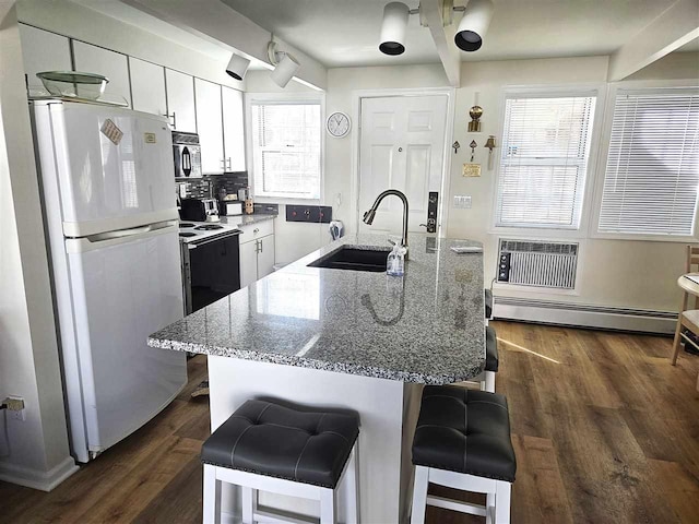 kitchen with a sink, a baseboard heating unit, a wall unit AC, freestanding refrigerator, and black microwave