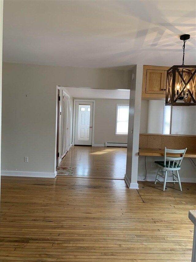 interior space with a notable chandelier, a baseboard radiator, baseboards, and wood finished floors