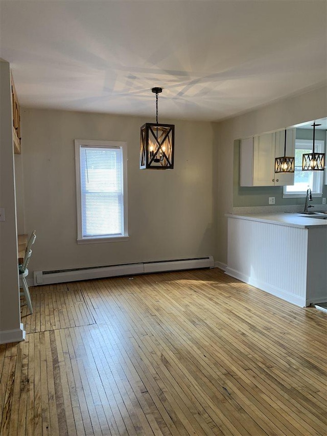 unfurnished dining area featuring a notable chandelier, light wood-style flooring, a sink, a baseboard heating unit, and a healthy amount of sunlight