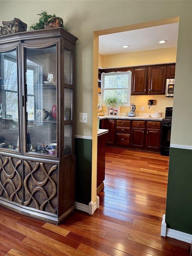 kitchen with stainless steel microwave, black gas stove, dark brown cabinetry, light countertops, and dark wood-style flooring