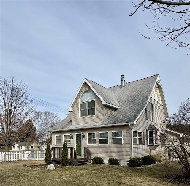 view of front of home with roof with shingles, a front lawn, and fence