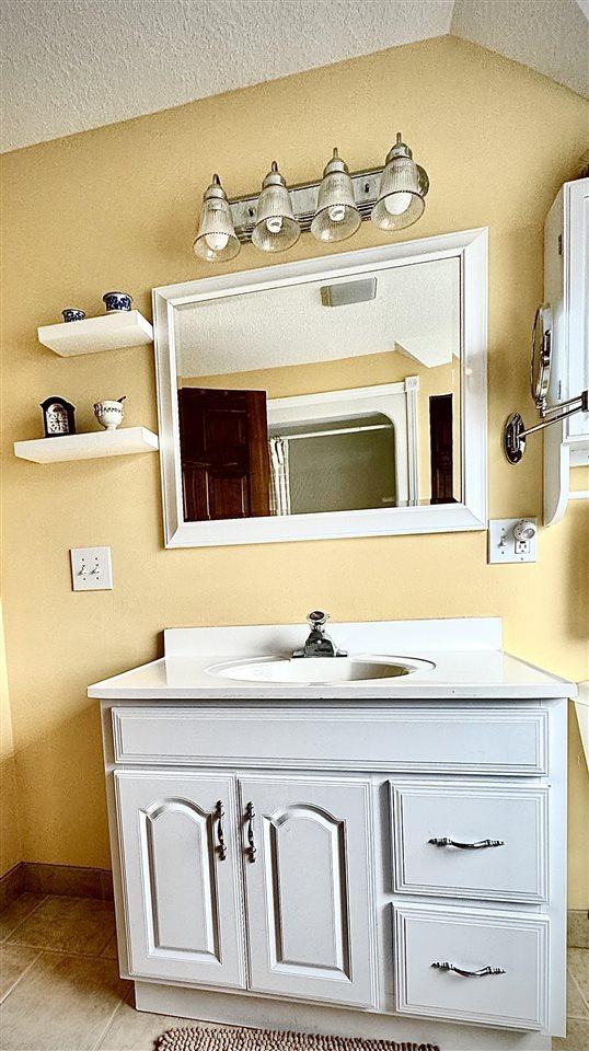 bathroom featuring tile patterned flooring, lofted ceiling, vanity, and baseboards