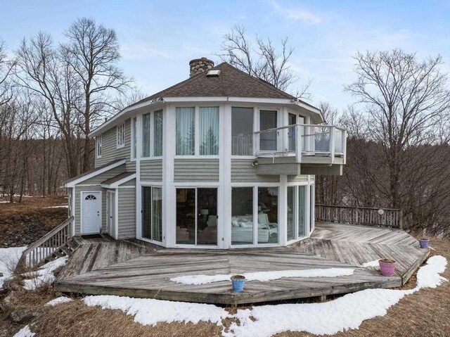1323 Charlevoix St, Boyne City, MI 49712 - snow covered back of property with a wooden deck, a balcony, a chimney, and roof with shingles