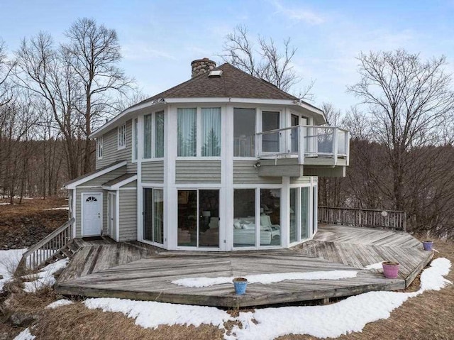 1323 Charlevoix St, Boyne City, MI 49712 - snow covered back of property with a wooden deck, a balcony, a chimney, and roof with shingles