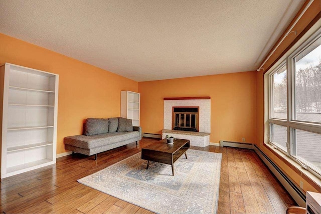 2382 Pleasant Valley Rd, Boyne City, MI 49712 - living area featuring baseboard heating, baseboards, a textured ceiling, a brick fireplace, and hardwood / wood-style flooring