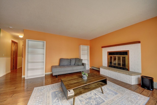 2382 Pleasant Valley Rd, Boyne City, MI 49712 - living room featuring a fireplace, a textured ceiling, a baseboard heating unit, baseboards, and hardwood / wood-style flooring