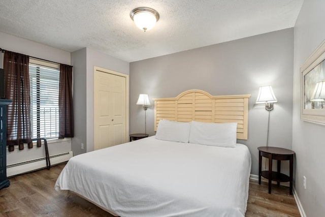 bedroom with a baseboard radiator, wood finished floors, baseboards, and a textured ceiling