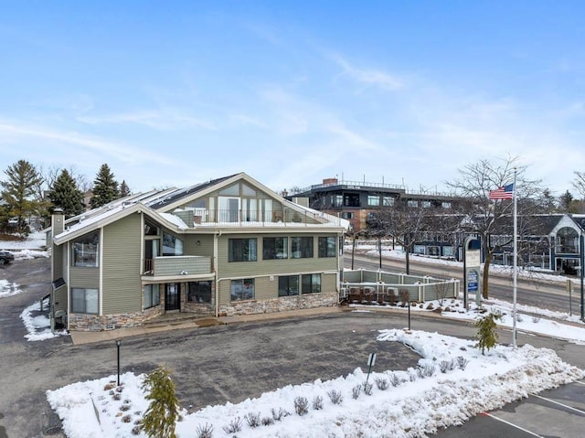 view of front of property with uncovered parking, fence, stone siding, and a balcony