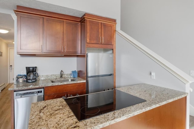 kitchen with a sink, light stone countertops, brown cabinets, and stainless steel appliances