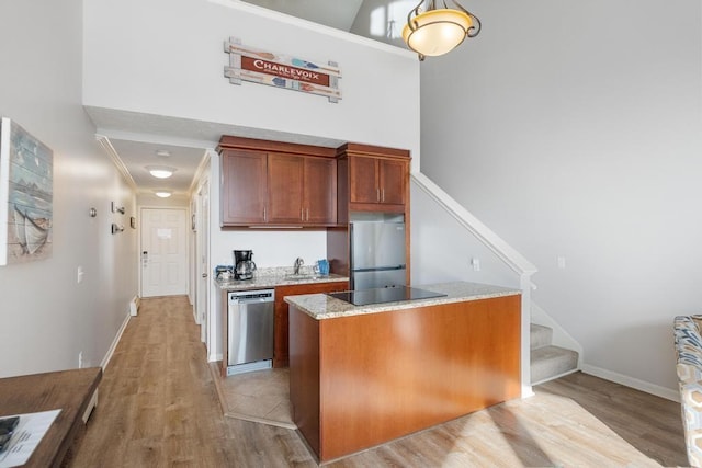 kitchen featuring a high ceiling, a sink, appliances with stainless steel finishes, light wood-style floors, and light stone countertops