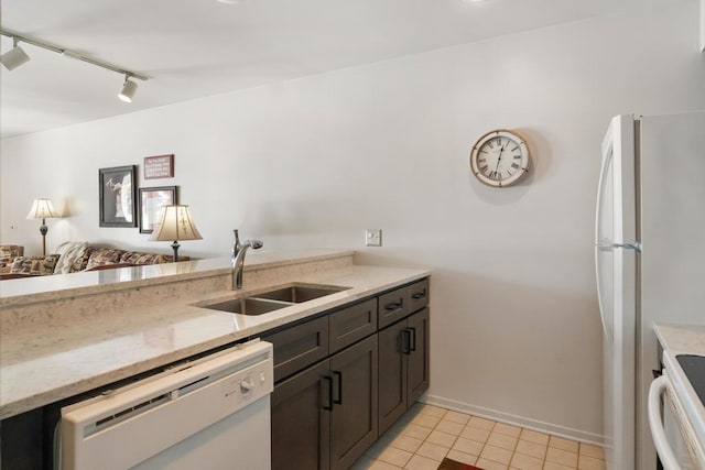 kitchen featuring track lighting, light tile patterned floors, a sink, white appliances, and light stone counters