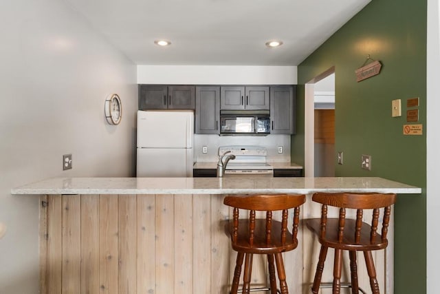 kitchen featuring light stone counters, white appliances, a kitchen bar, and a peninsula