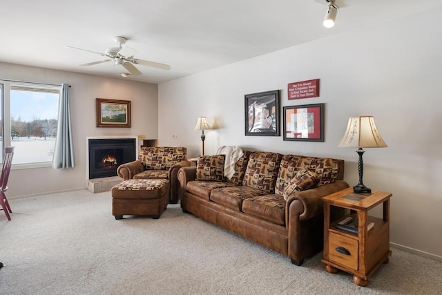 living area featuring ceiling fan, carpet, baseboards, and a lit fireplace