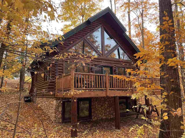 back of property featuring stone siding, log siding, and a deck