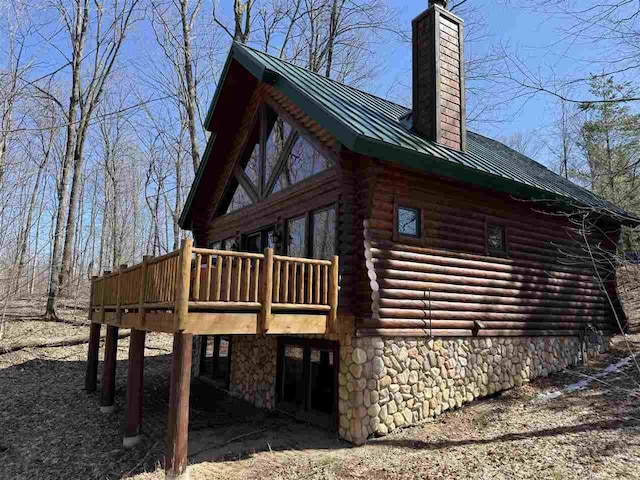 view of side of property featuring a chimney, metal roof, a wooden deck, log exterior, and a standing seam roof