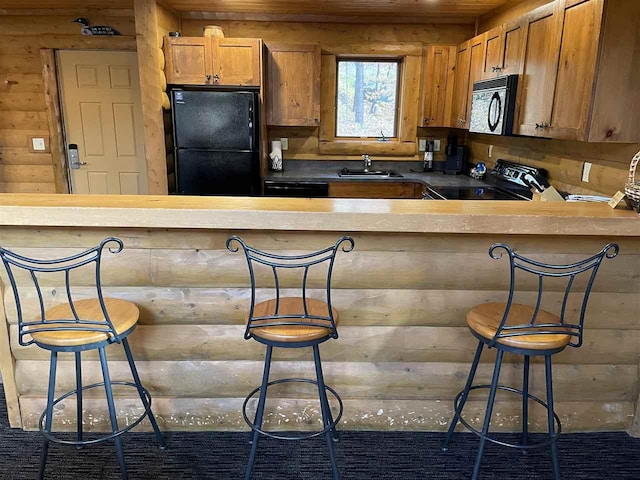 kitchen with a peninsula, a sink, a kitchen bar, brown cabinets, and black appliances