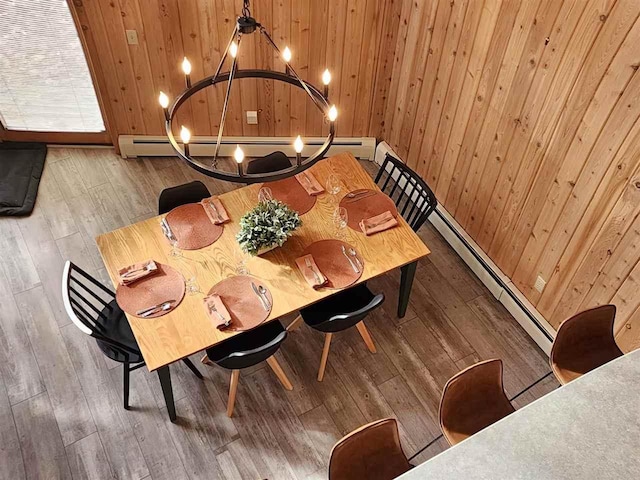dining room with baseboard heating, wood-type flooring, an inviting chandelier, and wood walls