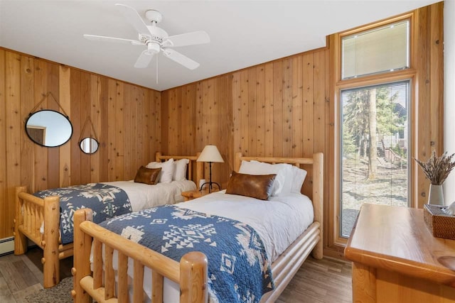 bedroom with a ceiling fan, wood finished floors, and wooden walls