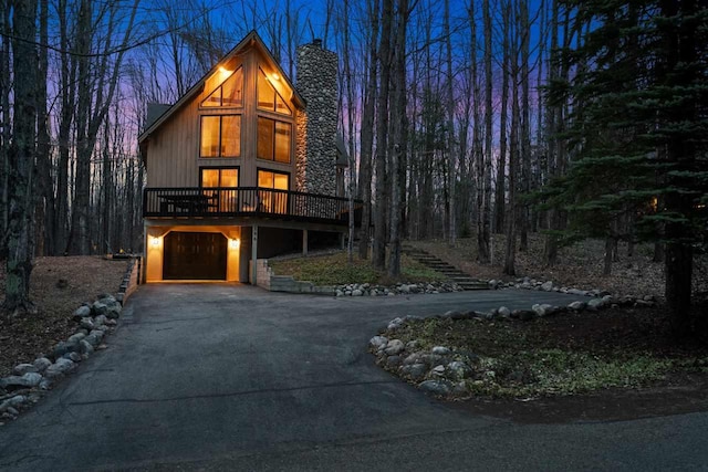 view of front of property featuring a chimney, a garage, stairway, a deck, and aphalt driveway
