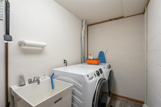 clothes washing area with independent washer and dryer, wood finished floors, laundry area, and a sink
