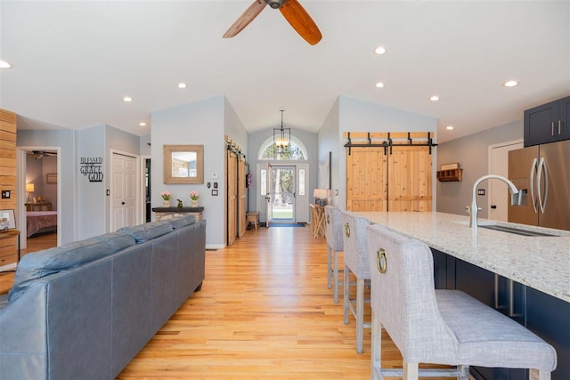 6001 N Silver Pines Dr, Bellaire, MI 49615 - kitchen featuring a barn door, vaulted ceiling, a breakfast bar, light wood-style flooring, and stainless steel refrigerator with ice dispenser