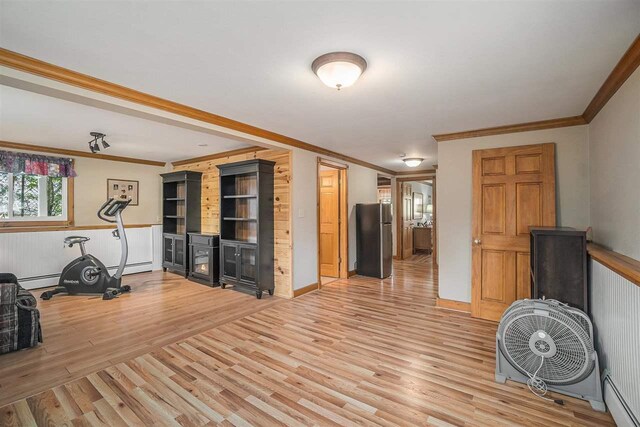 exercise area with a baseboard heating unit, a wainscoted wall, wood finished floors, and crown molding