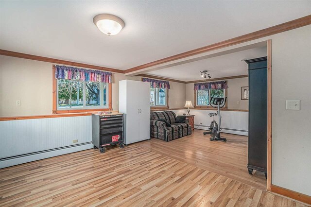 interior space with a baseboard heating unit, wood finished floors, crown molding, and a wainscoted wall