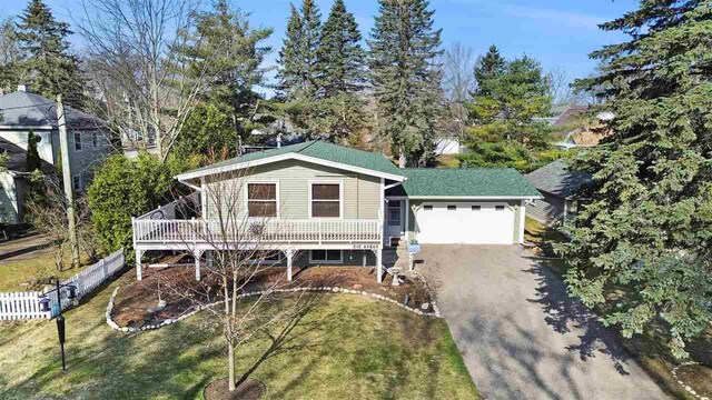 view of front of property featuring a deck, fence, driveway, a front yard, and an attached garage