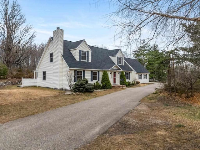cape cod home featuring a shingled roof, a chimney, and aphalt driveway