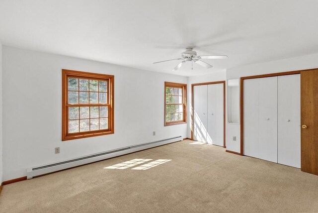 unfurnished bedroom featuring a baseboard heating unit, multiple closets, carpet flooring, and multiple windows