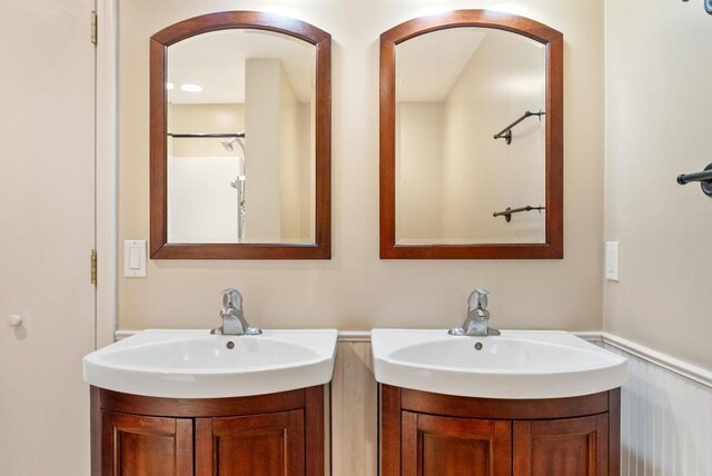 bathroom featuring two vanities, wainscoting, and a sink