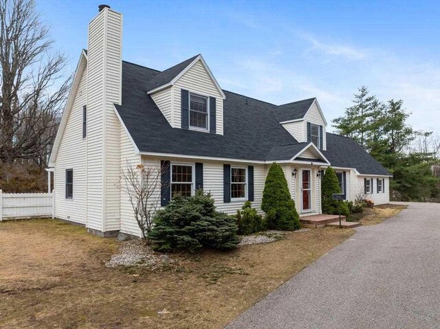 cape cod home featuring a chimney and fence