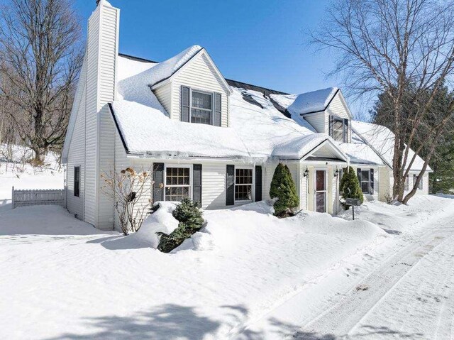 cape cod-style house featuring a chimney and fence