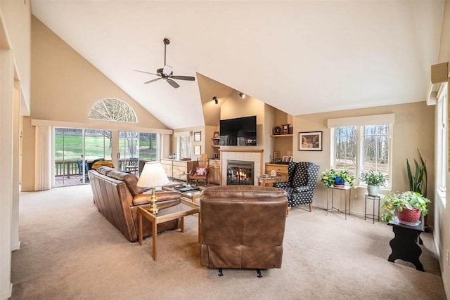 living area featuring ceiling fan, a healthy amount of sunlight, light carpet, a fireplace, and high vaulted ceiling