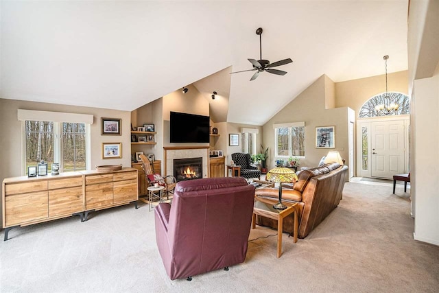 living area featuring ceiling fan with notable chandelier, high vaulted ceiling, light carpet, and a tiled fireplace