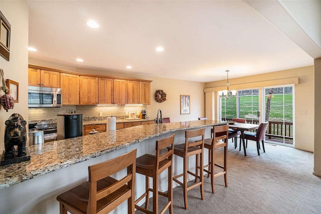 kitchen with a breakfast bar area, stainless steel appliances, light stone countertops, light carpet, and backsplash