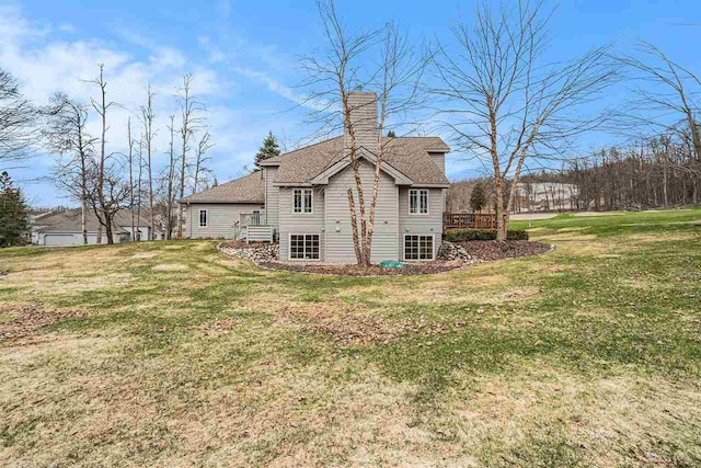 back of property featuring a chimney, a yard, and roof with shingles