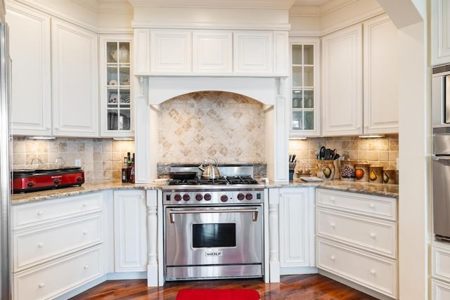 kitchen with tasteful backsplash, light stone countertops, high end stainless steel range, white cabinets, and dark wood-style floors