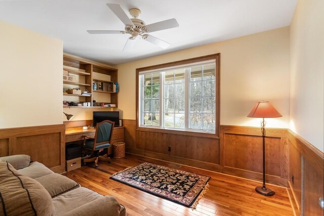 office with a ceiling fan, wood walls, light wood-style flooring, and a wainscoted wall