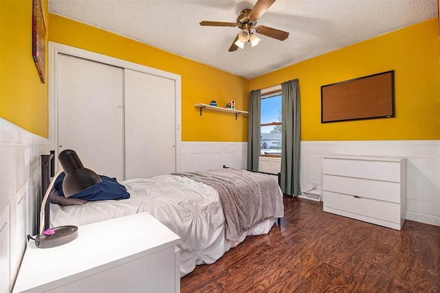 11601 Sequanota Heights Dr, Charlevoix, MI 49720 - bedroom with a textured ceiling, ceiling fan, a wainscoted wall, a closet, and dark wood-style flooring