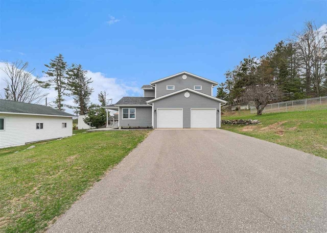 traditional home with an attached garage, a front lawn, fence, and driveway