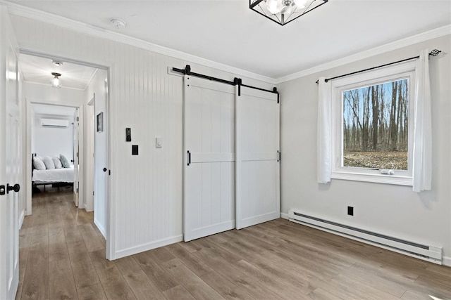 unfurnished bedroom featuring crown molding, baseboard heating, light wood-type flooring, a barn door, and a wall mounted air conditioner