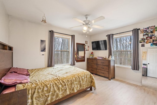 bedroom with baseboards, ceiling fan, multiple windows, and light wood-style flooring