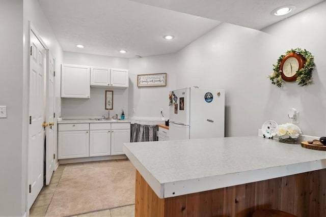 kitchen with a sink, light countertops, light tile patterned floors, freestanding refrigerator, and a peninsula