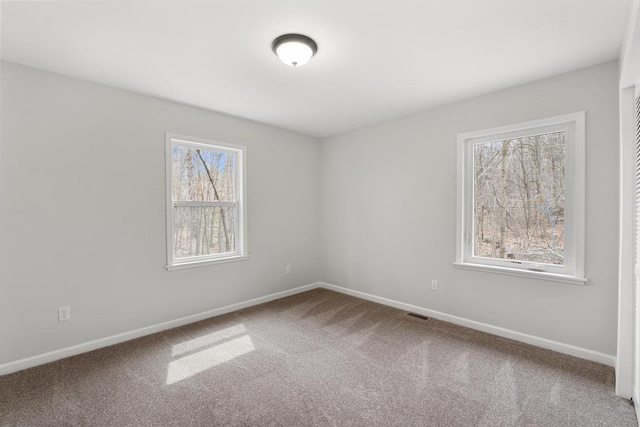 carpeted spare room featuring baseboards, a wealth of natural light, and visible vents