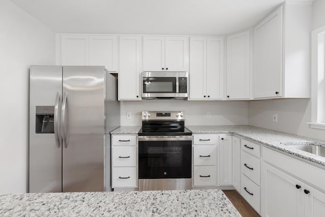 kitchen with light stone counters, dark wood finished floors, appliances with stainless steel finishes, and white cabinets