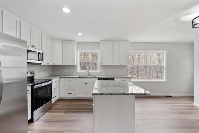 kitchen featuring appliances with stainless steel finishes, a center island, a sink, baseboards, and light stone counters