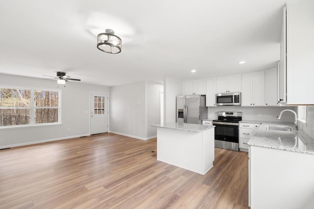 kitchen with a ceiling fan, a center island, a sink, stainless steel appliances, and light wood-style flooring