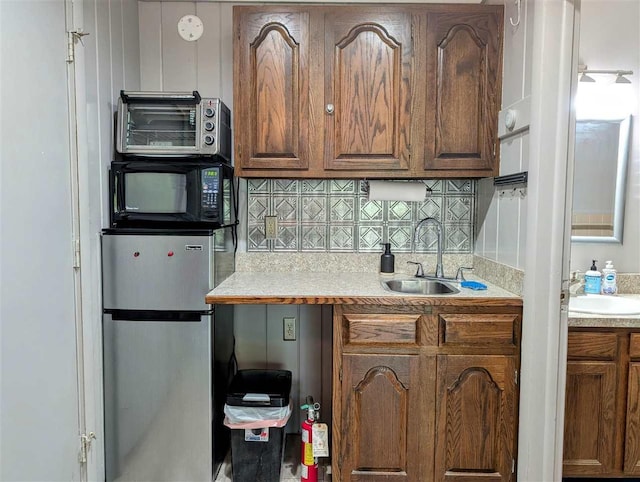 kitchen featuring black microwave, freestanding refrigerator, backsplash, and a sink