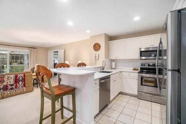 kitchen with appliances with stainless steel finishes, a breakfast bar, a sink, a peninsula, and white cabinetry